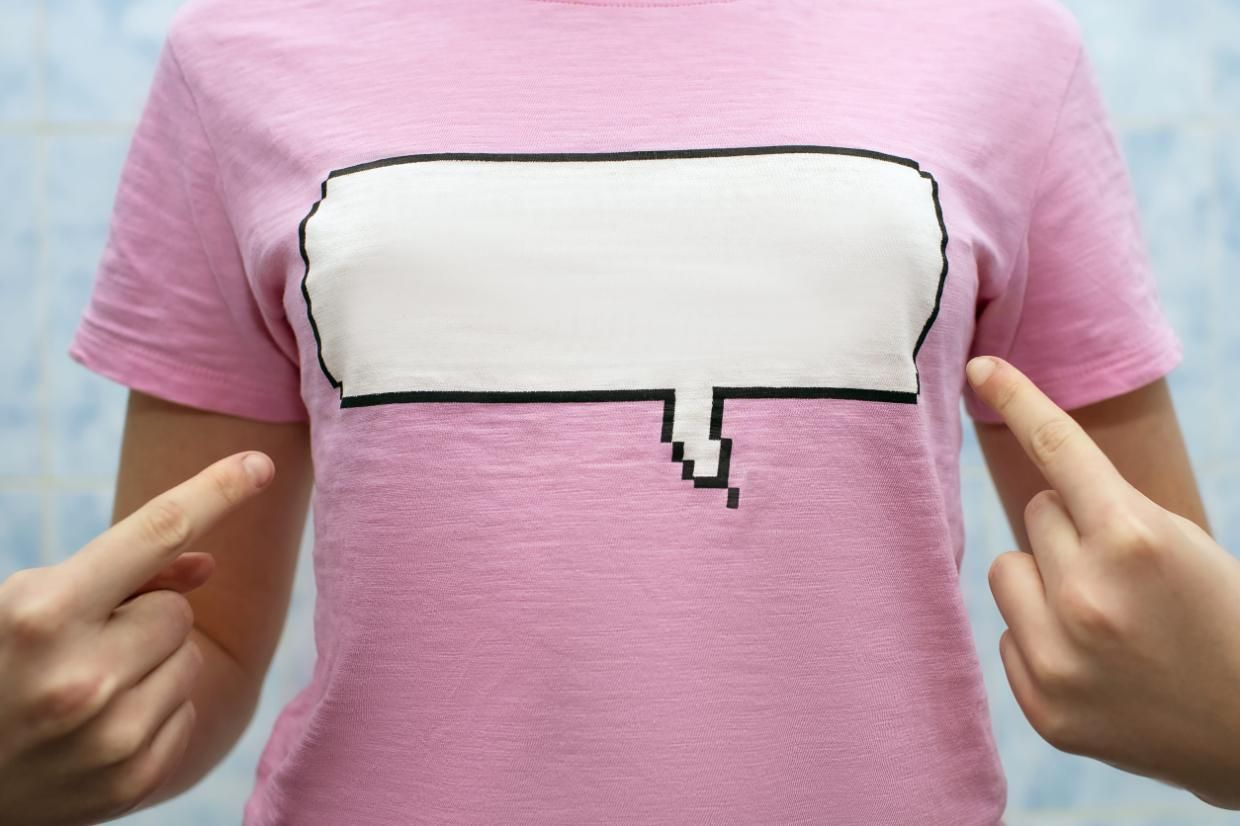 Persona con una camisa rosa con un gráfico de una burbuja de diálogo blanca y dos dedos apuntando hacia ella.