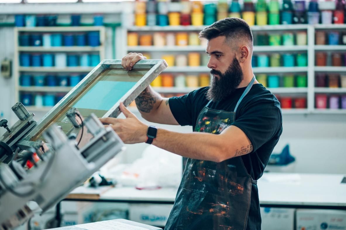 Un hombre examina un bastidor de serigrafía en una colorida imprenta.