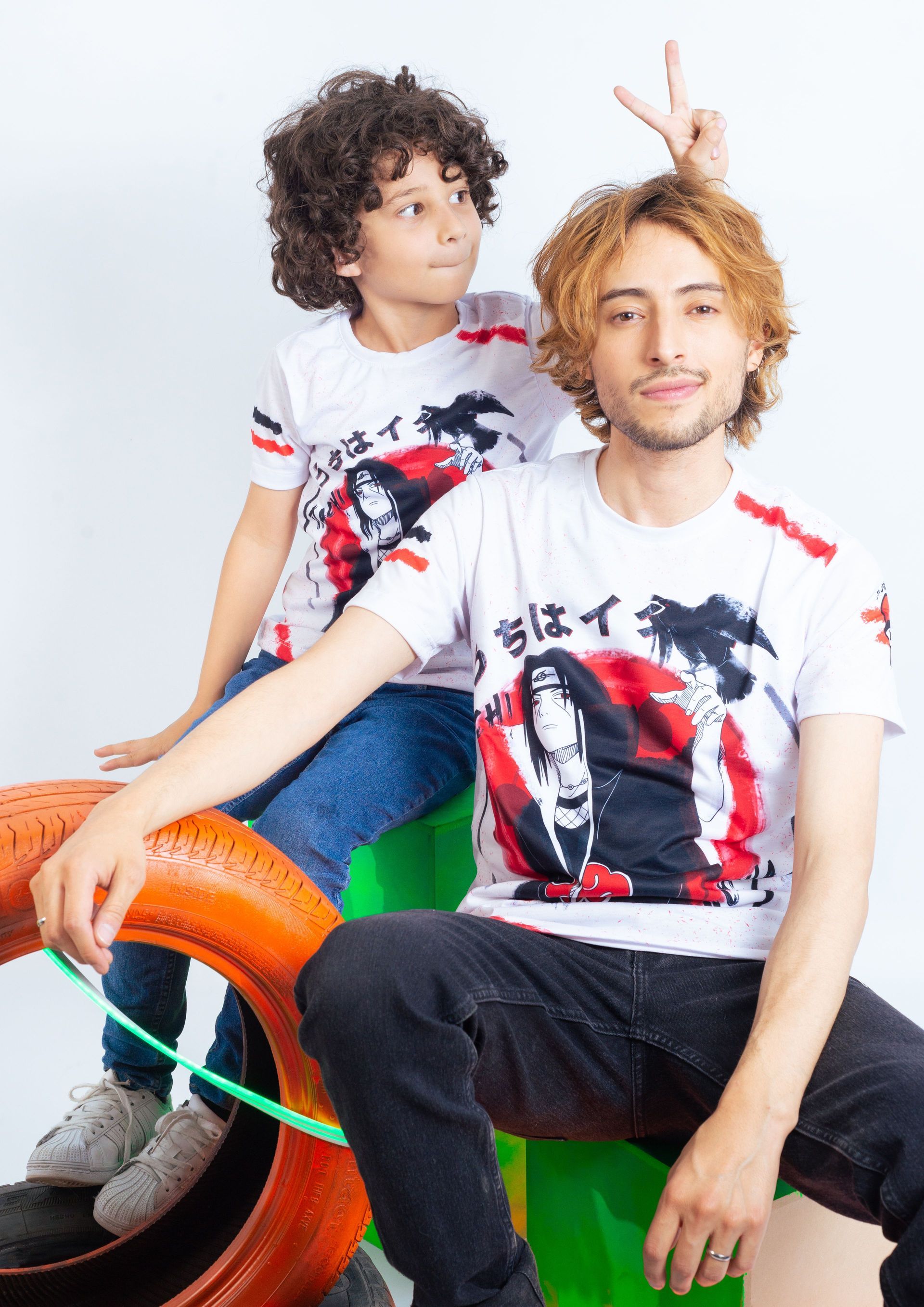 Dos personas con camisetas estampadas a juego están sentadas en una silla colorida sobre un fondo blanco.
