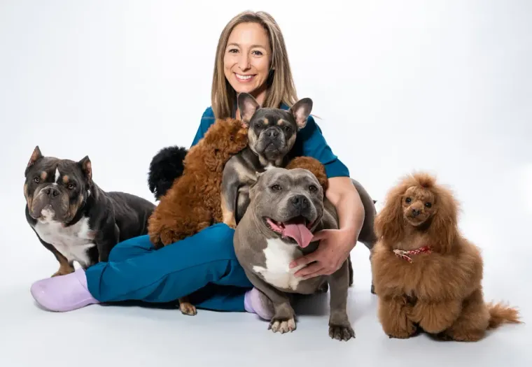Mujer sonríe, rodeada de seis perros, sobre fondo blanco.