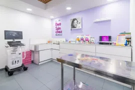 Sala de examen de clínica veterinaria con ecógrafo, mesa de acero inoxidable y mostrador de exhibición de productos