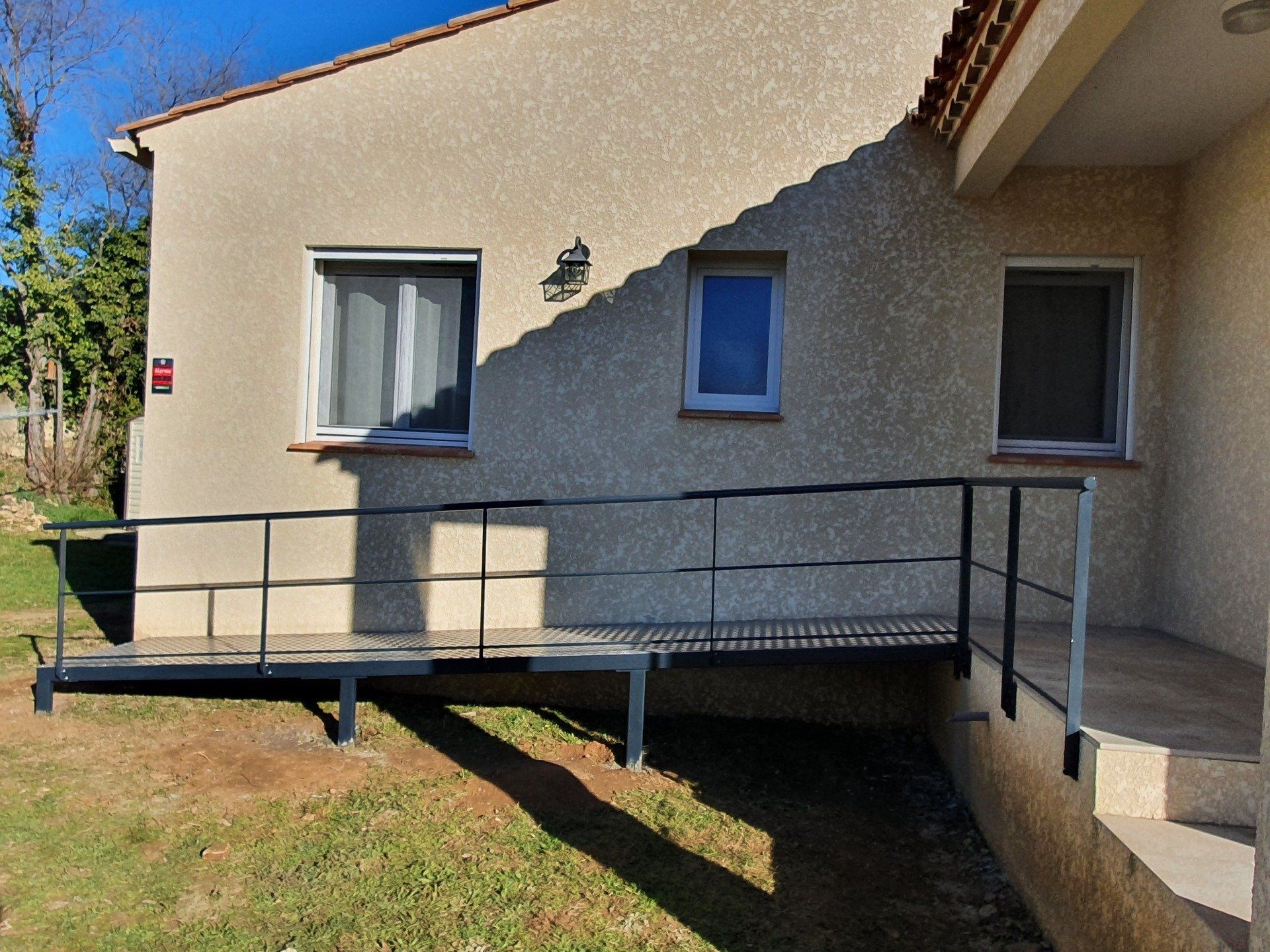 Rampe métallique d'accès pour fauteuil roulant menant à un bâtiment clair avec des fenêtres.