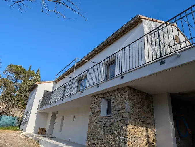 Bâtiment blanc de deux étages avec des éléments en pierre, un balcon et un ciel bleu.