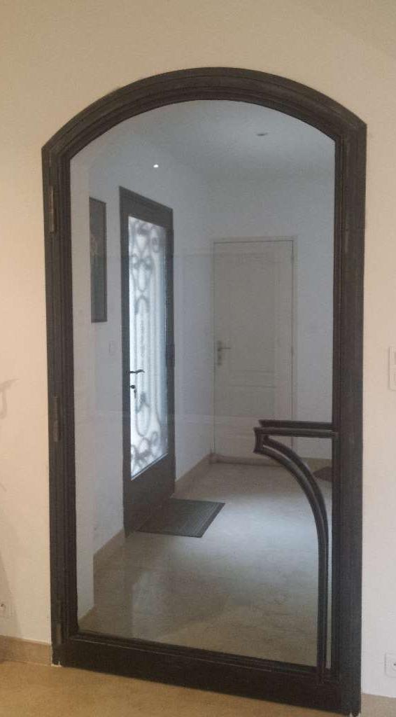 Porte moustiquaire cintrée à cadre sombre dans un couloir, reflétant une porte, un sol et un intérieur.