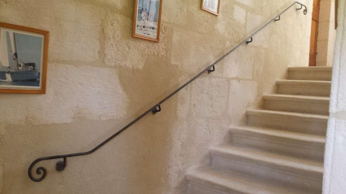 Escalier avec une rampe en métal noir contre un mur en pierre claire.