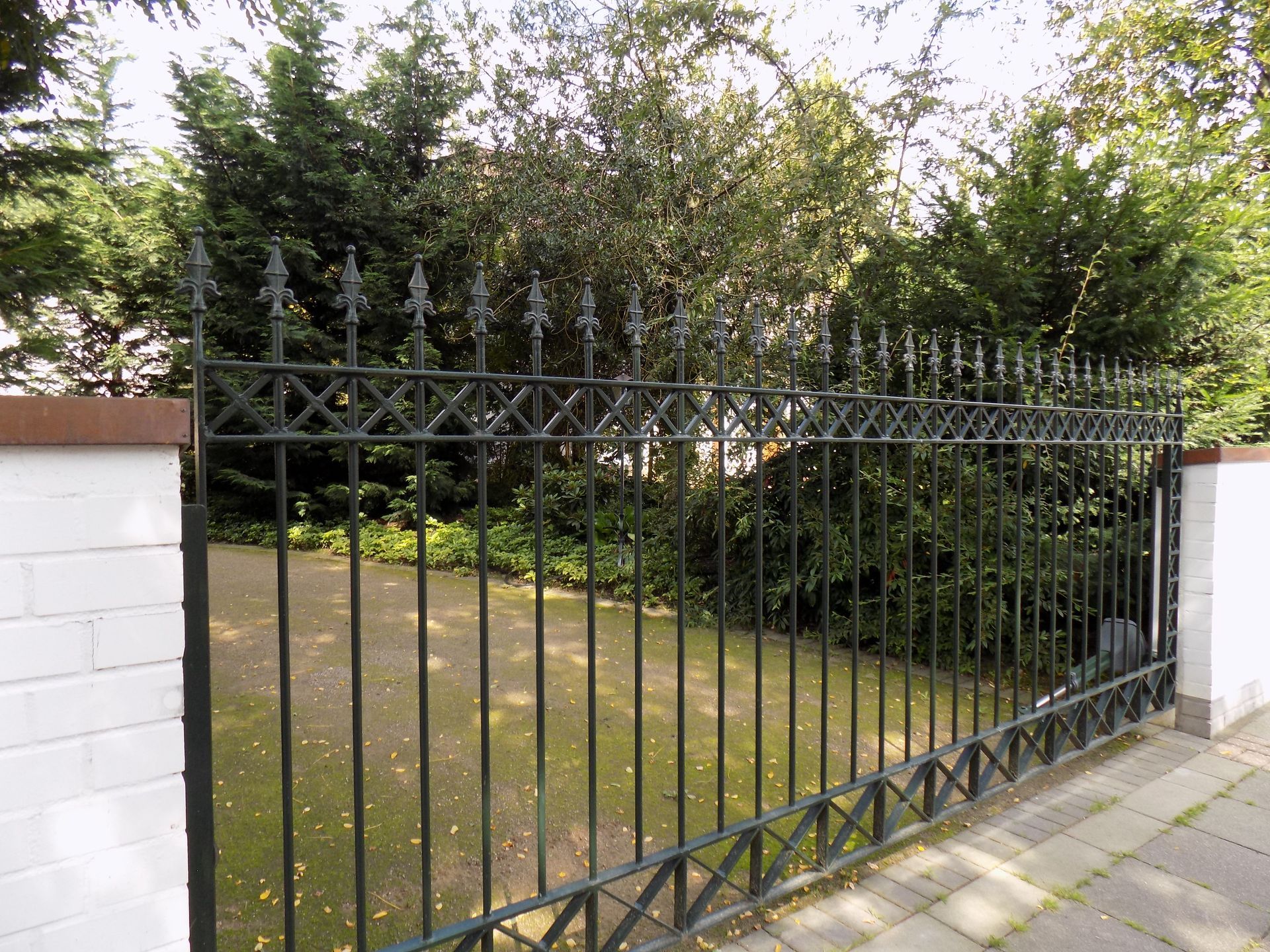 Ein schmiedeeisernes Tor ist von Bäumen und einer weißen Wand umgeben