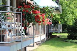 Ein Balkon mit hängenden roten Blumen neben einem Haus.