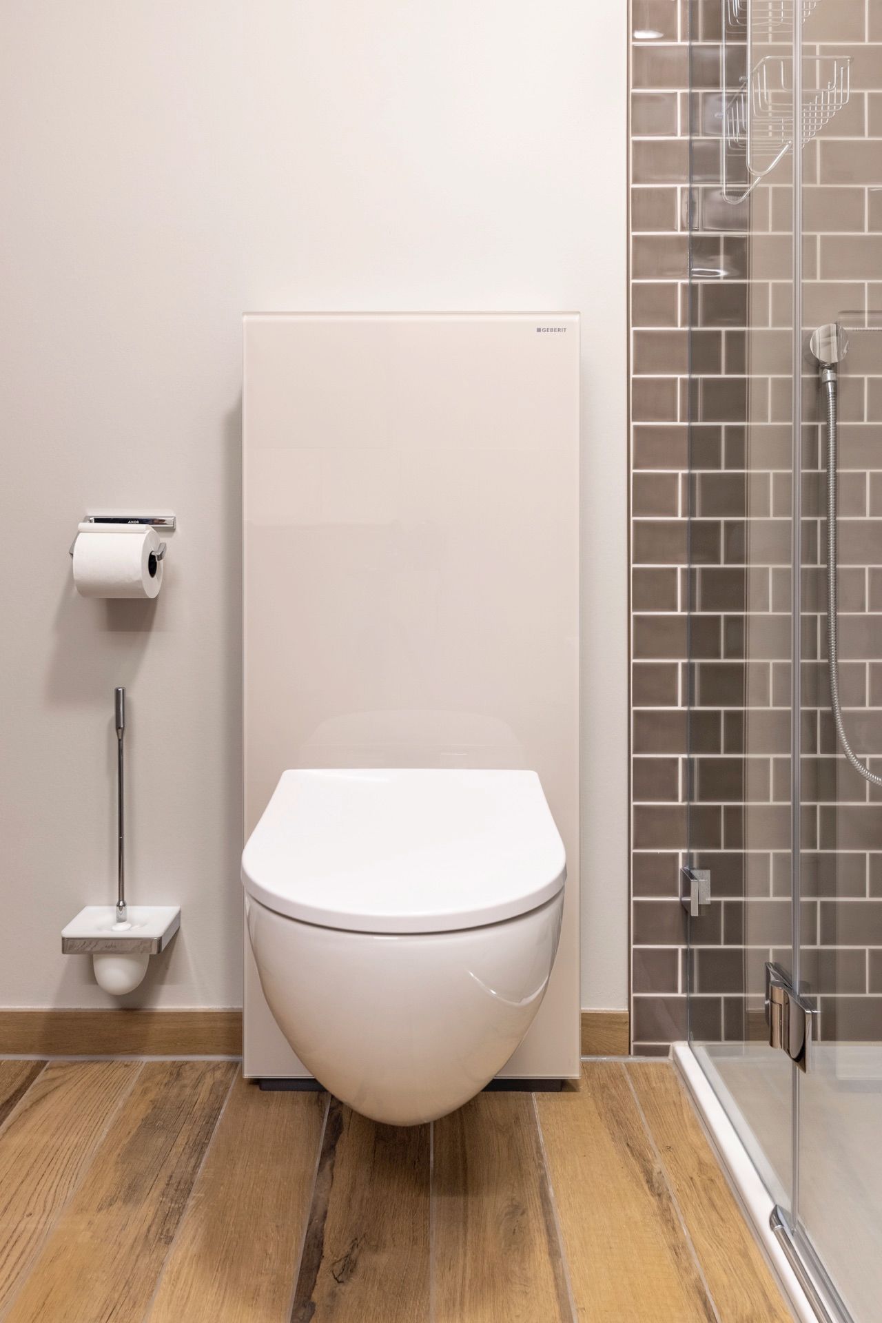 In einem Badezimmer hängt neben einer Dusche eine Toilette an der Wand.