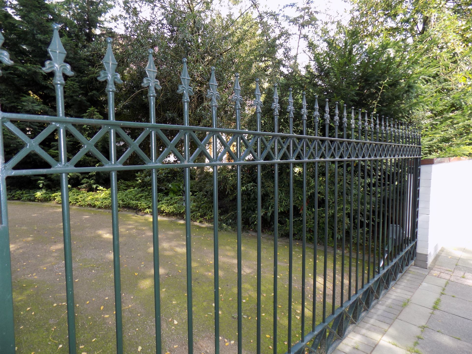 Ein grüner schmiedeeiserner Zaun ist von Bäumen umgeben