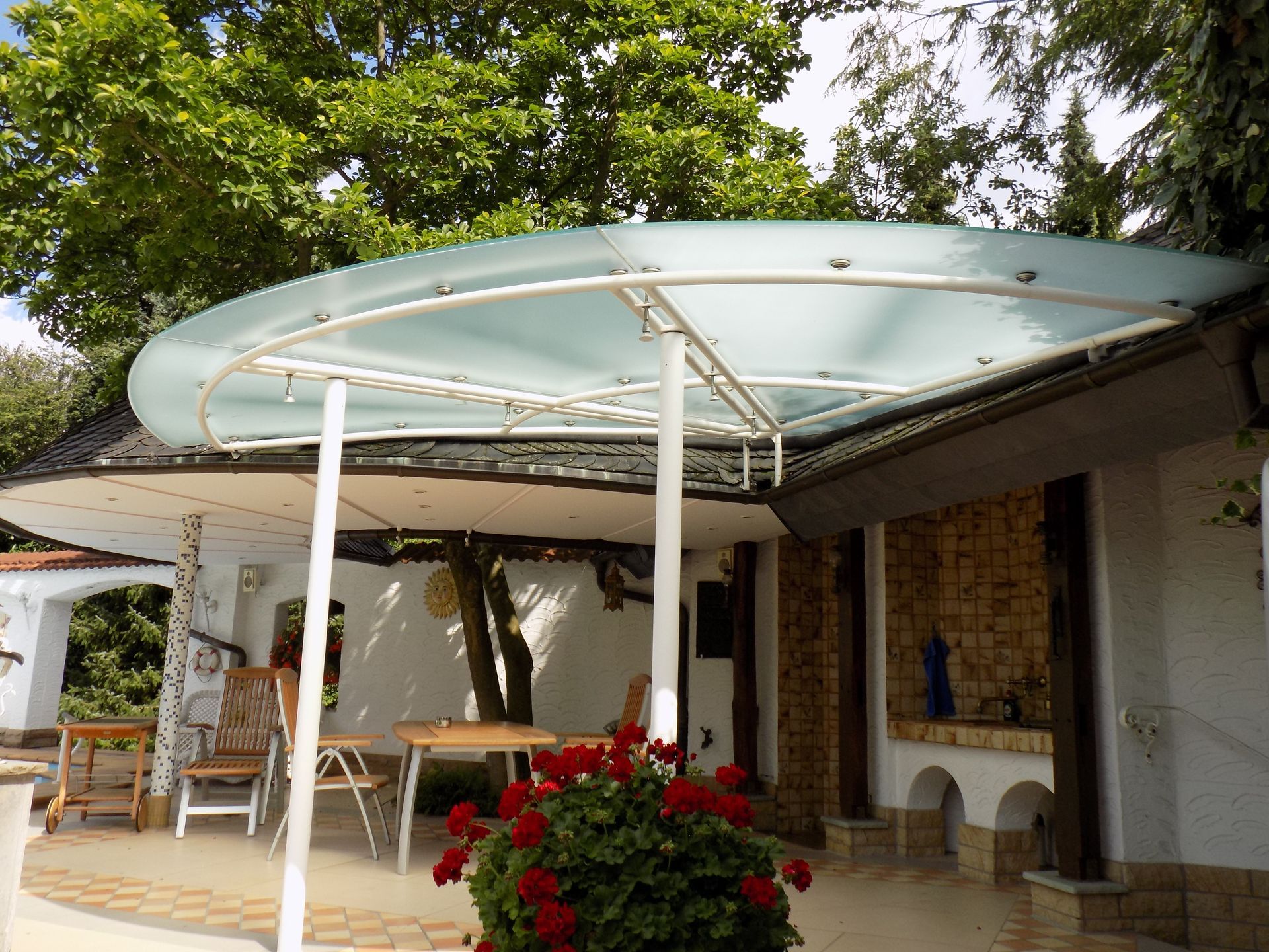 Ein Glasdach über einer Terrasse mit Tisch und Stühlen