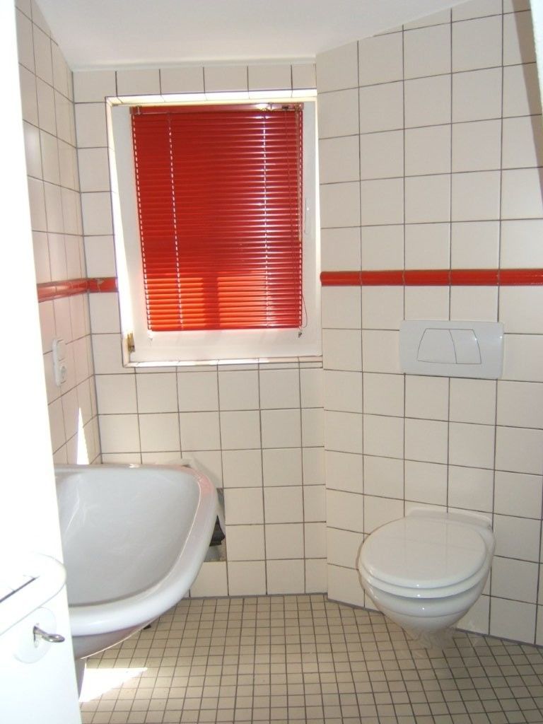 Ein Badezimmer mit weißen Fliesen und roten Jalousien
