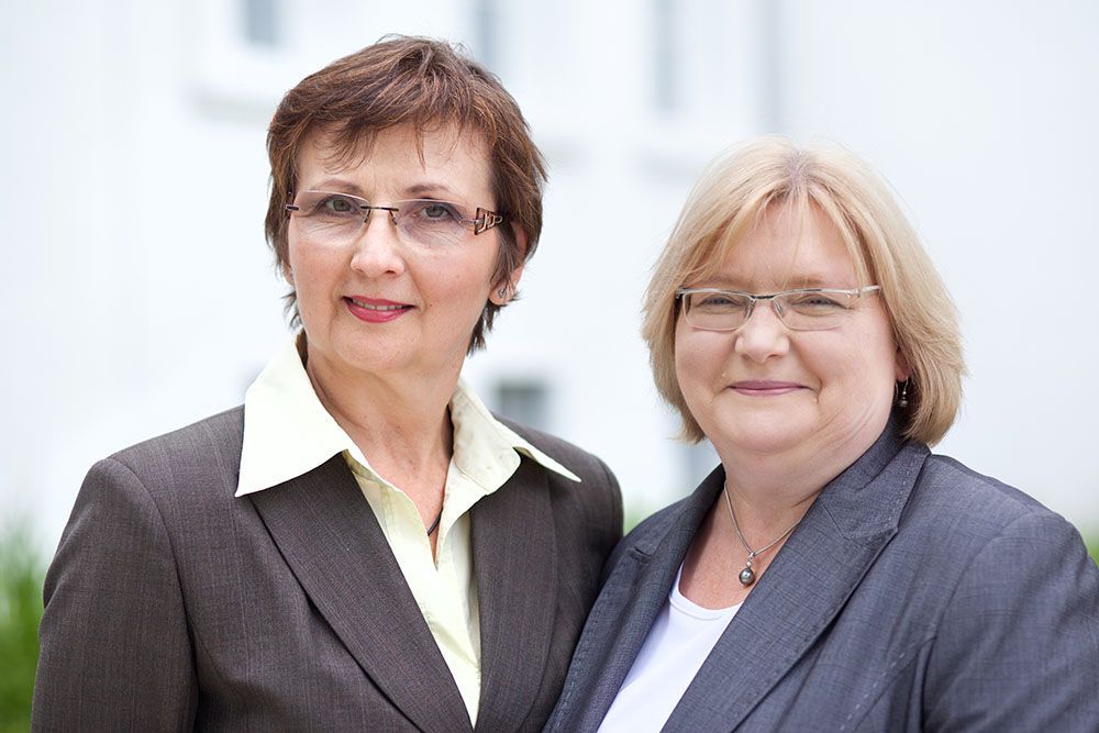 Zwei Frauen in Anzug und Brille posieren für ein Foto