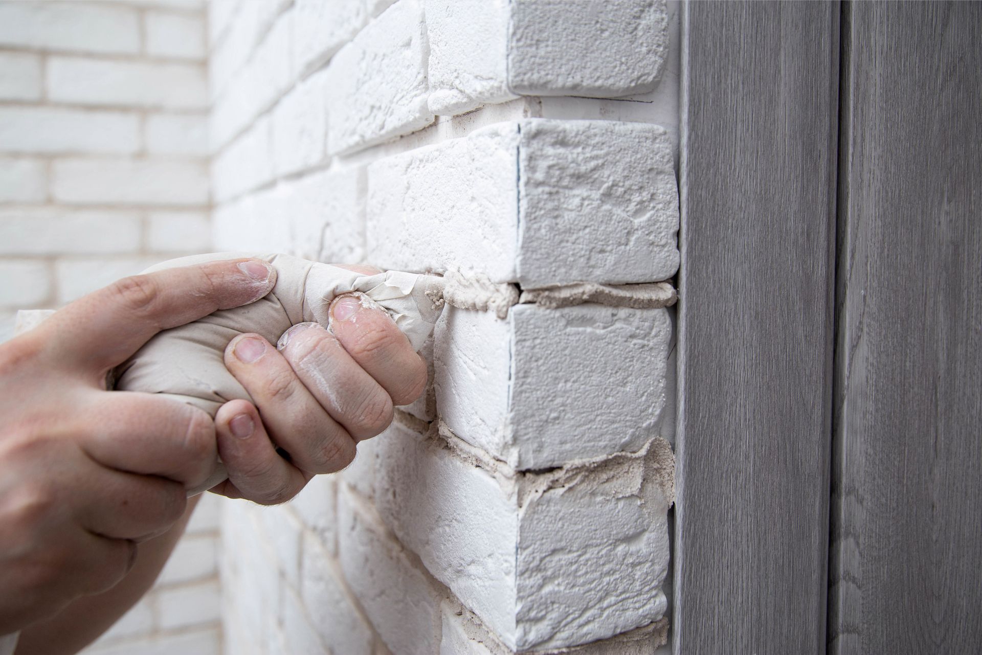 Gros plan sur la main d'un homme qui pose un joint sur mur de briques