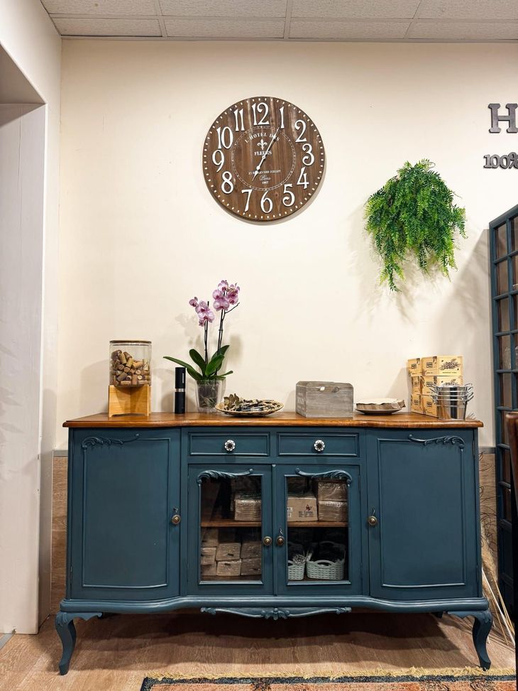 Aparador vintage azul con plantas, jarrones y un reloj de pared en un interior acogedor.