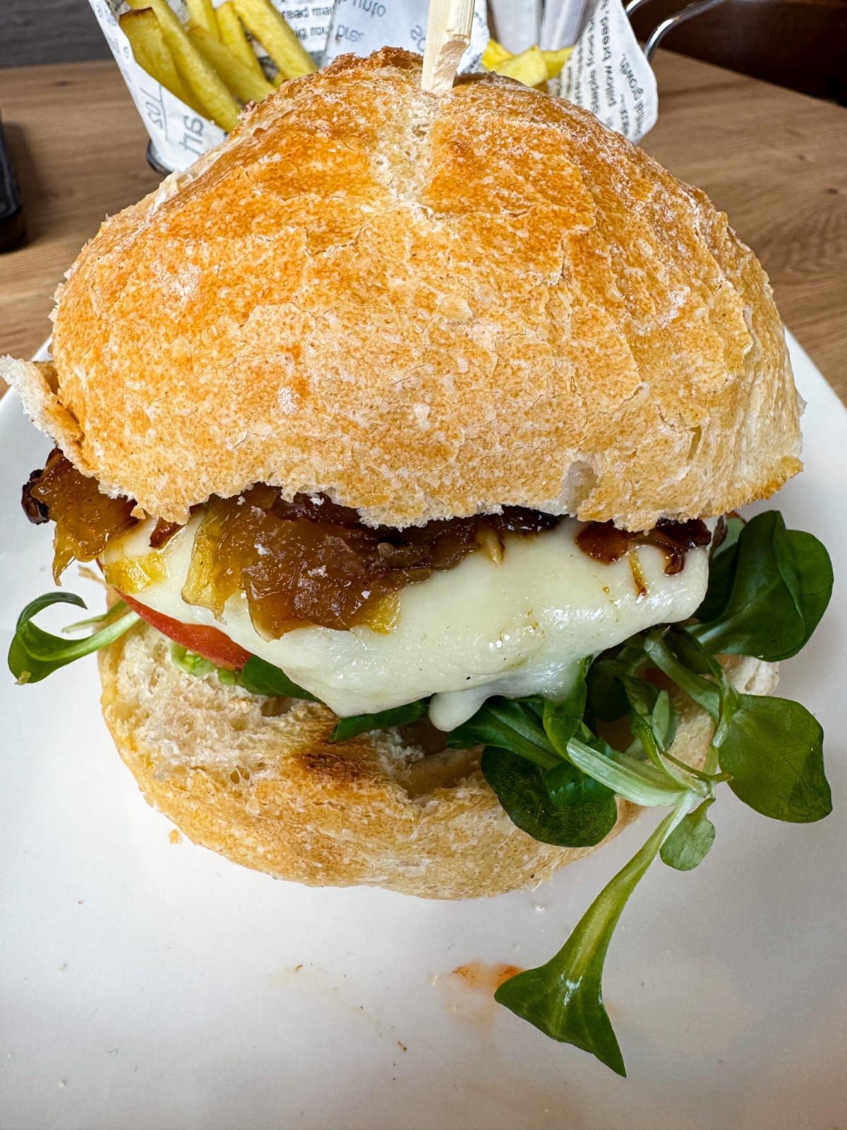 Primer plano de una hamburguesa crujiente empanizada con queso derretido, verduras y salsa en un plato blanco.