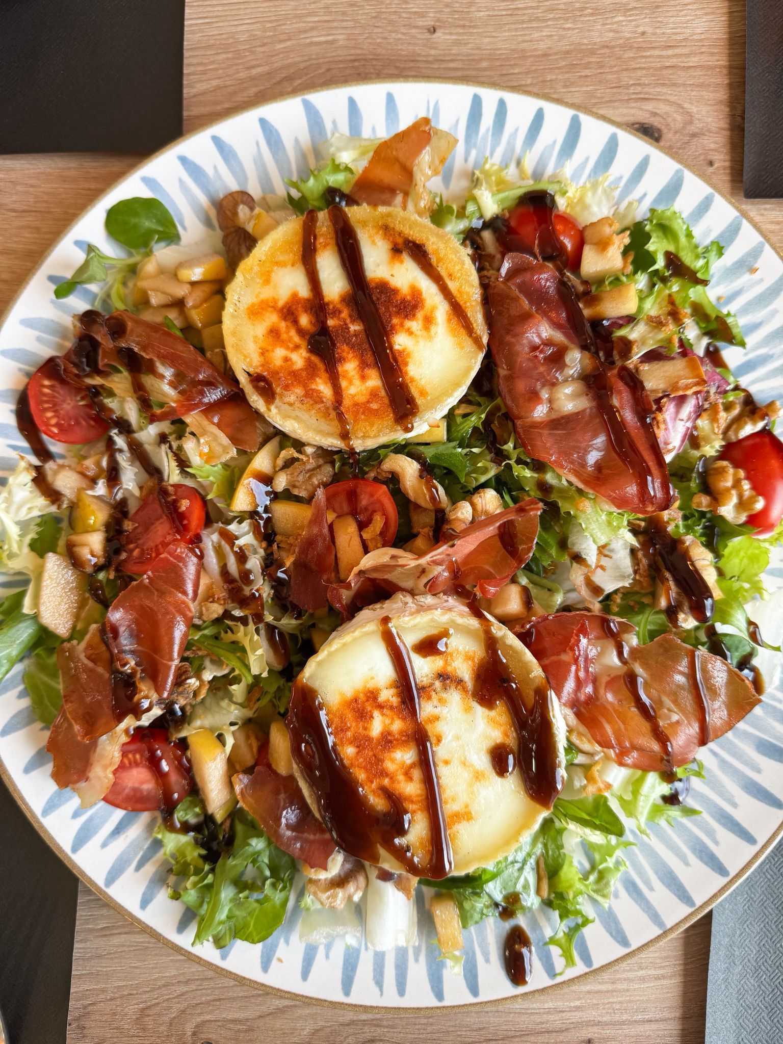 Ensalada emplatada con duraznos a la parrilla, jamón serrano y hojas verdes en un plato blanco.