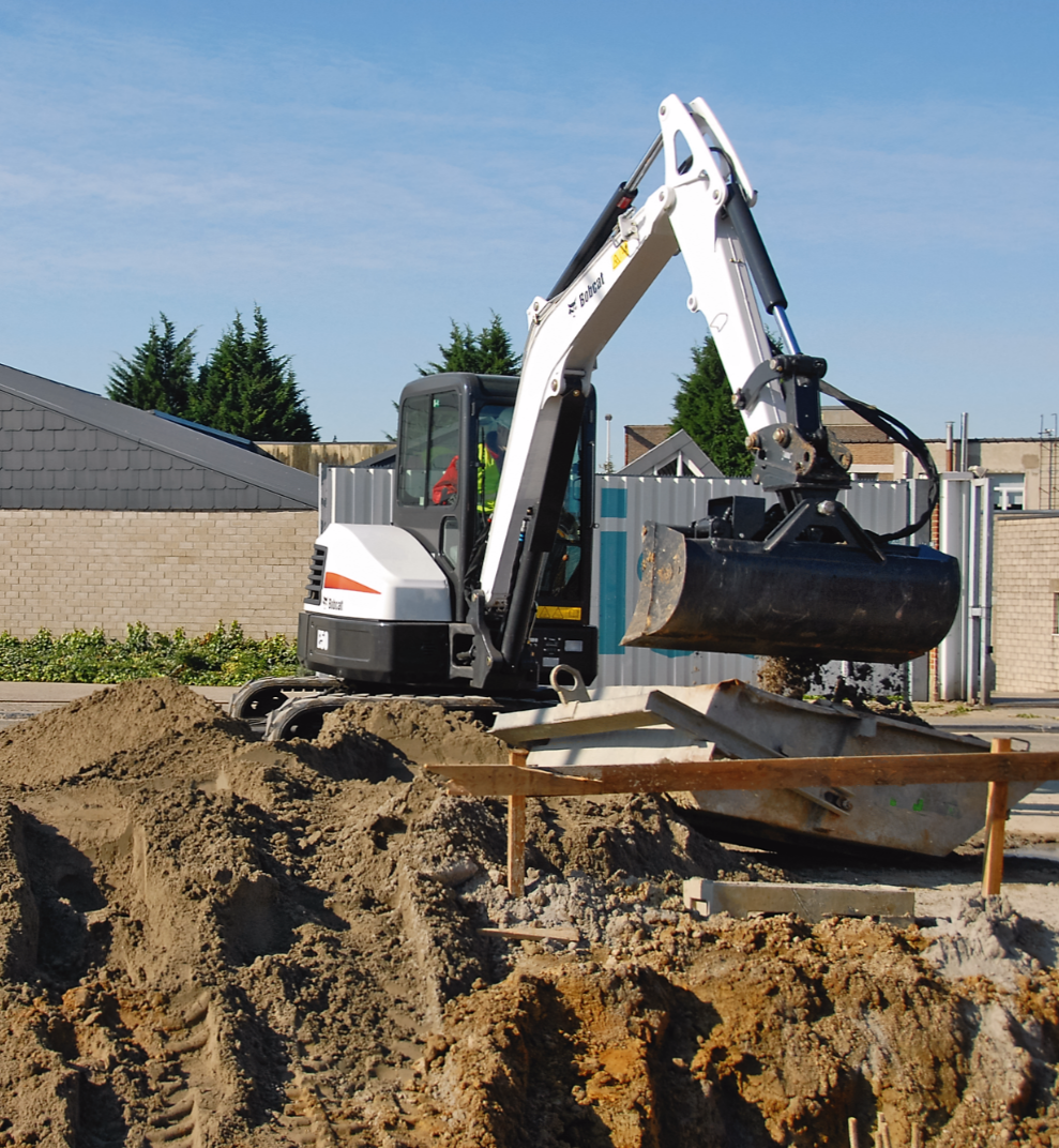 Une petite excavatrice creuse un tas de terre, préparant un chantier de construction.