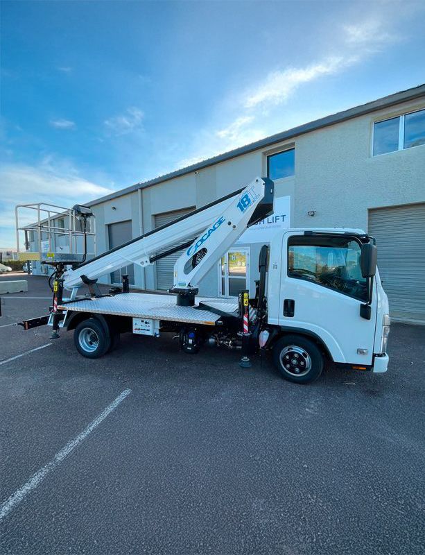 Camion Isuzu blanc avec hayon élévateur hydraulique, stationné devant un bâtiment.