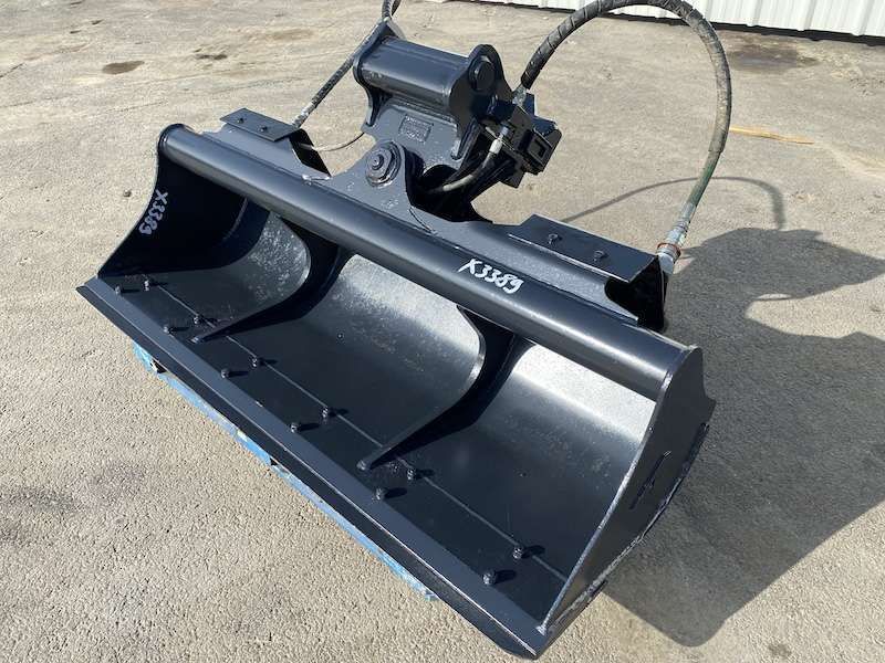 Godet d'excavatrice noir avec flexibles hydrauliques, à l'extérieur sur du béton.