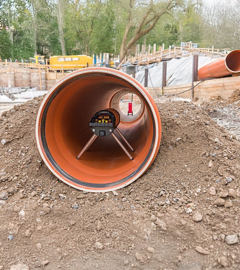 Gros tuyau orange contenant du matériel de topographie, posé sur un tas de terre sur un chantier de construction.