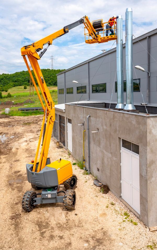 Une nacelle élévatrice jaune se déploie vers un bâtiment ; une personne dans la nacelle travaille sur une cheminée.
