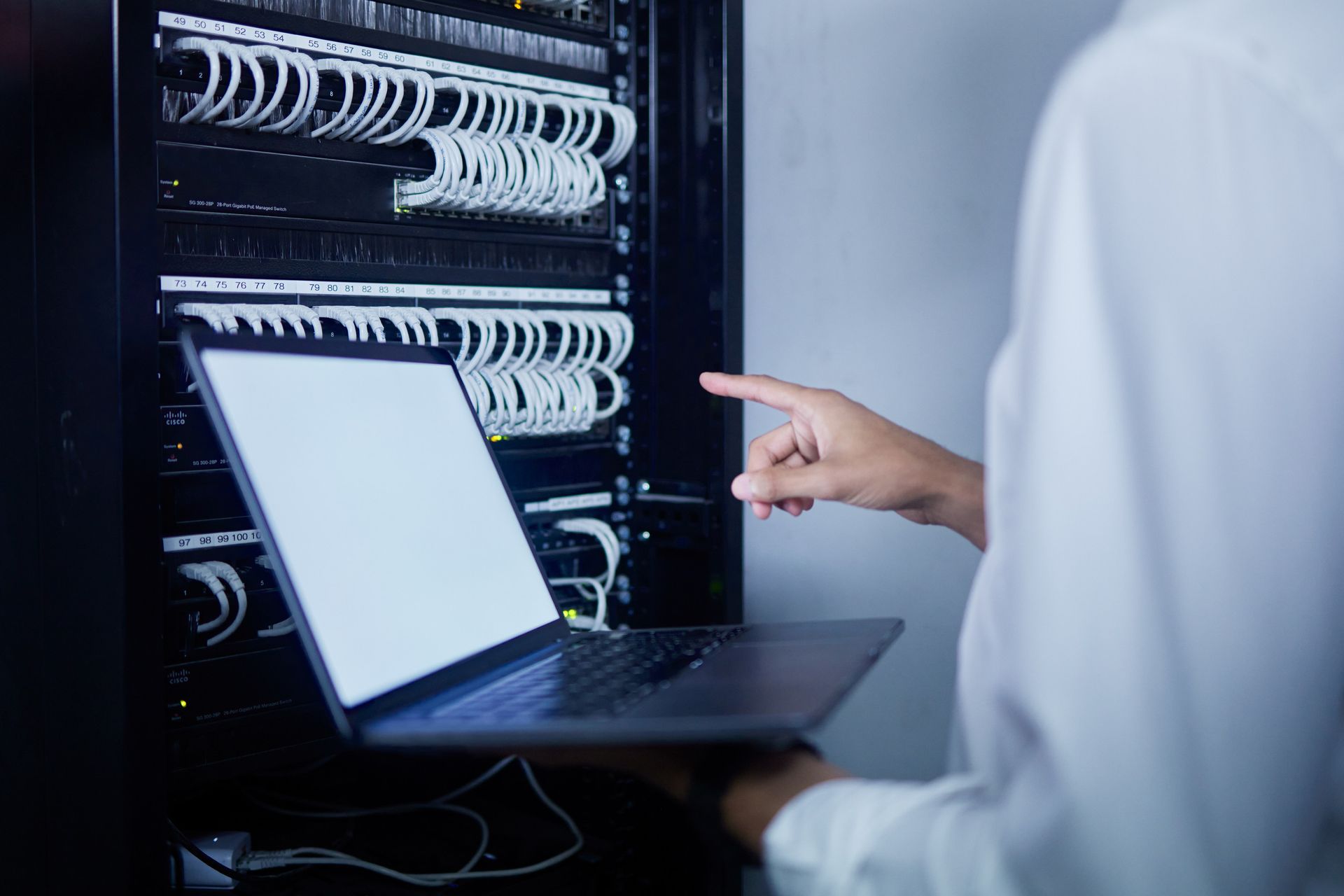 Una persona señala una computadora portátil en una sala de servidores.