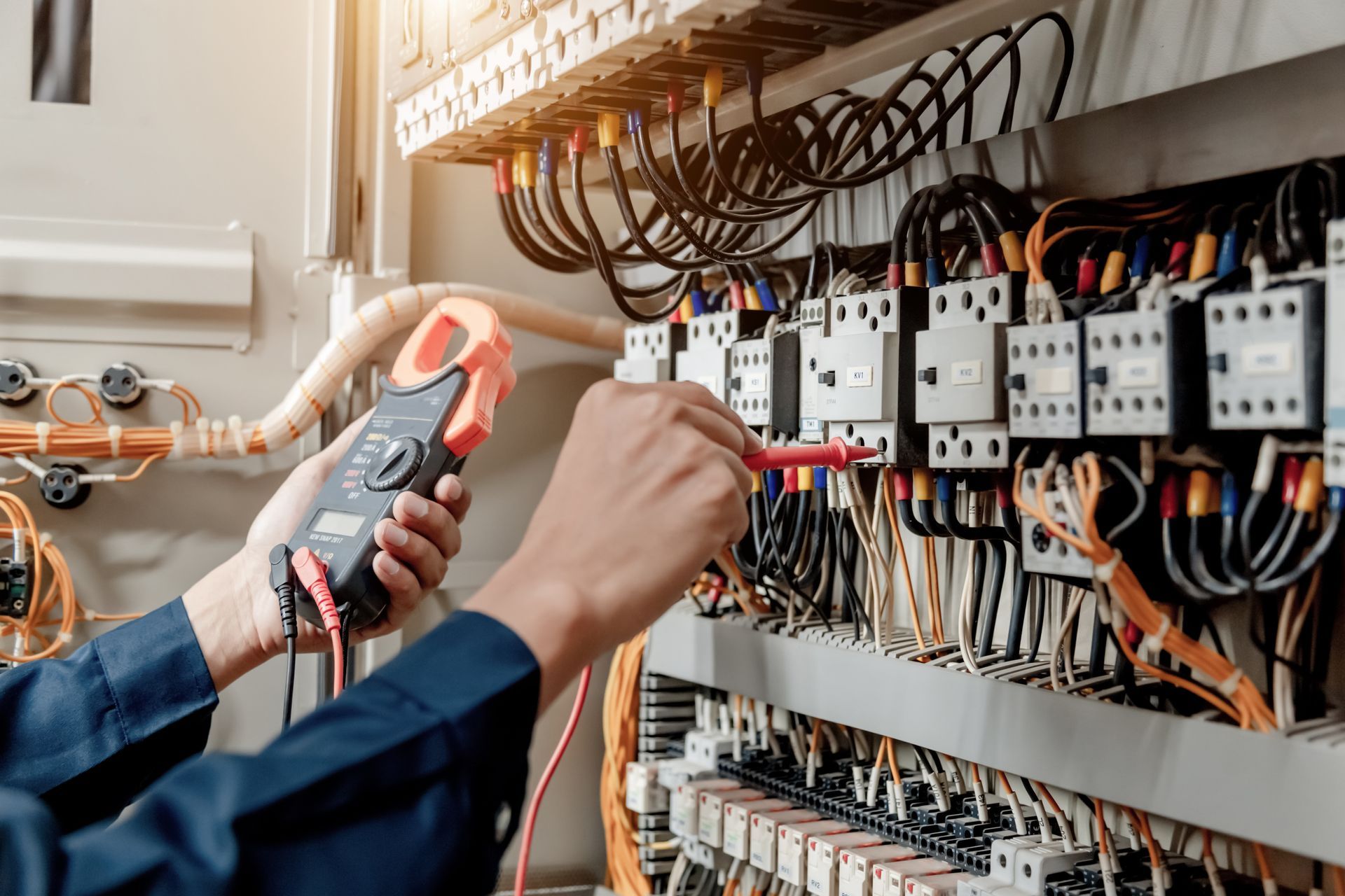 Techniker schneidet mit einer Zange Drähte im Inneren eines elektrischen Schaltschranks durch.