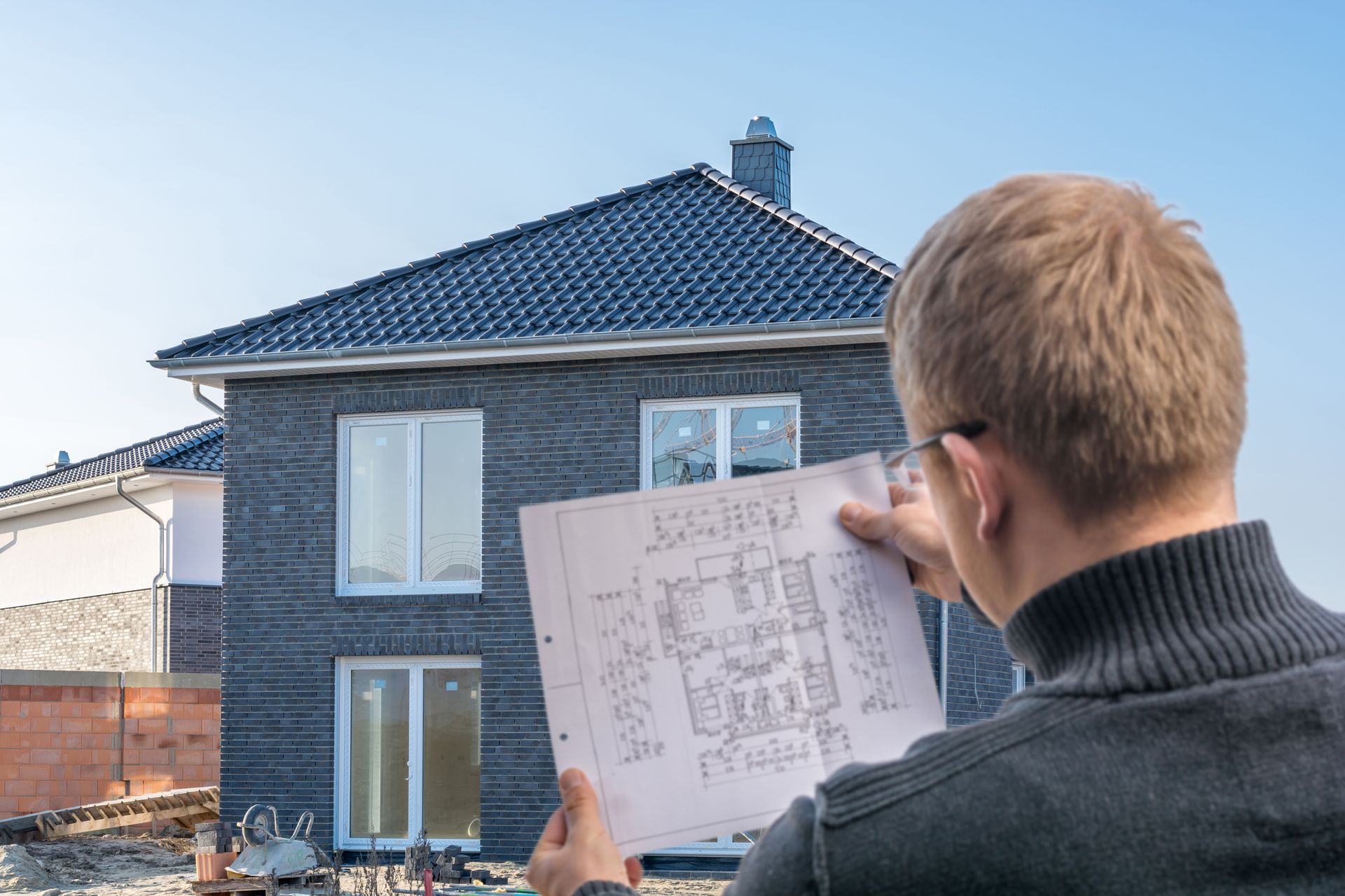 Une personne examine les plans d'une maison en briques grises nouvellement construite.