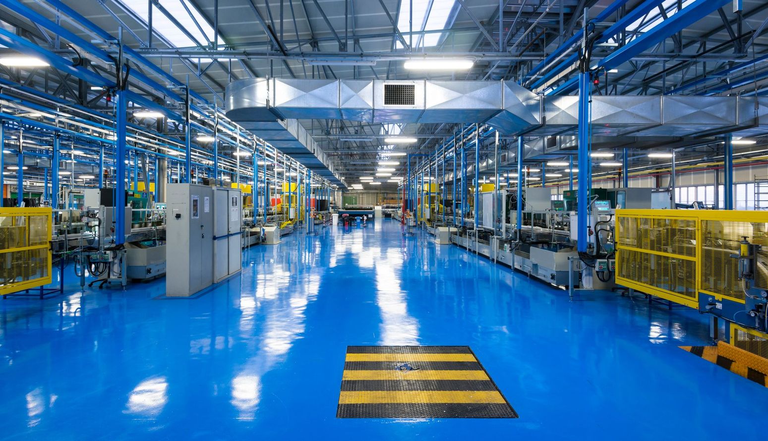 Sol d'usine lumineux avec béton poli bleu, machines industrielles et poutres d'acier au plafond.