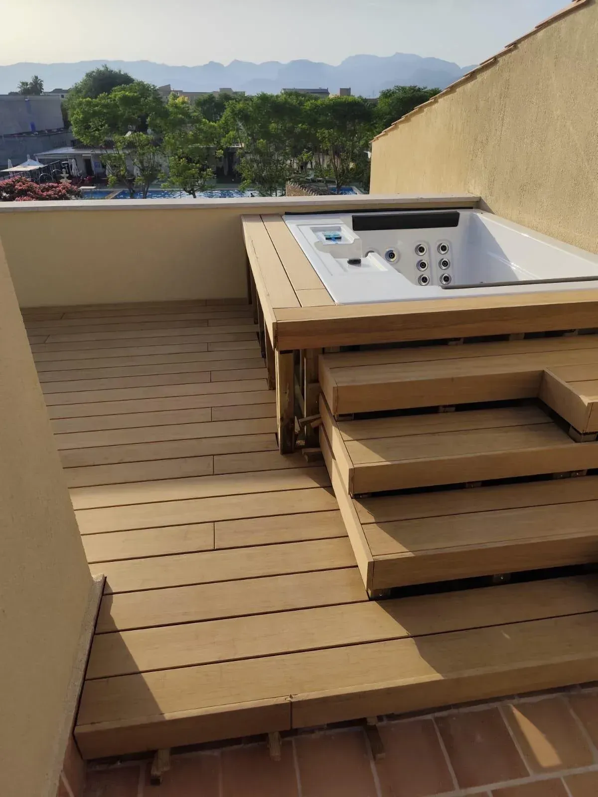 Terraza exterior de madera con jacuzzi incorporado, escalones y vistas a la montaña al fondo.