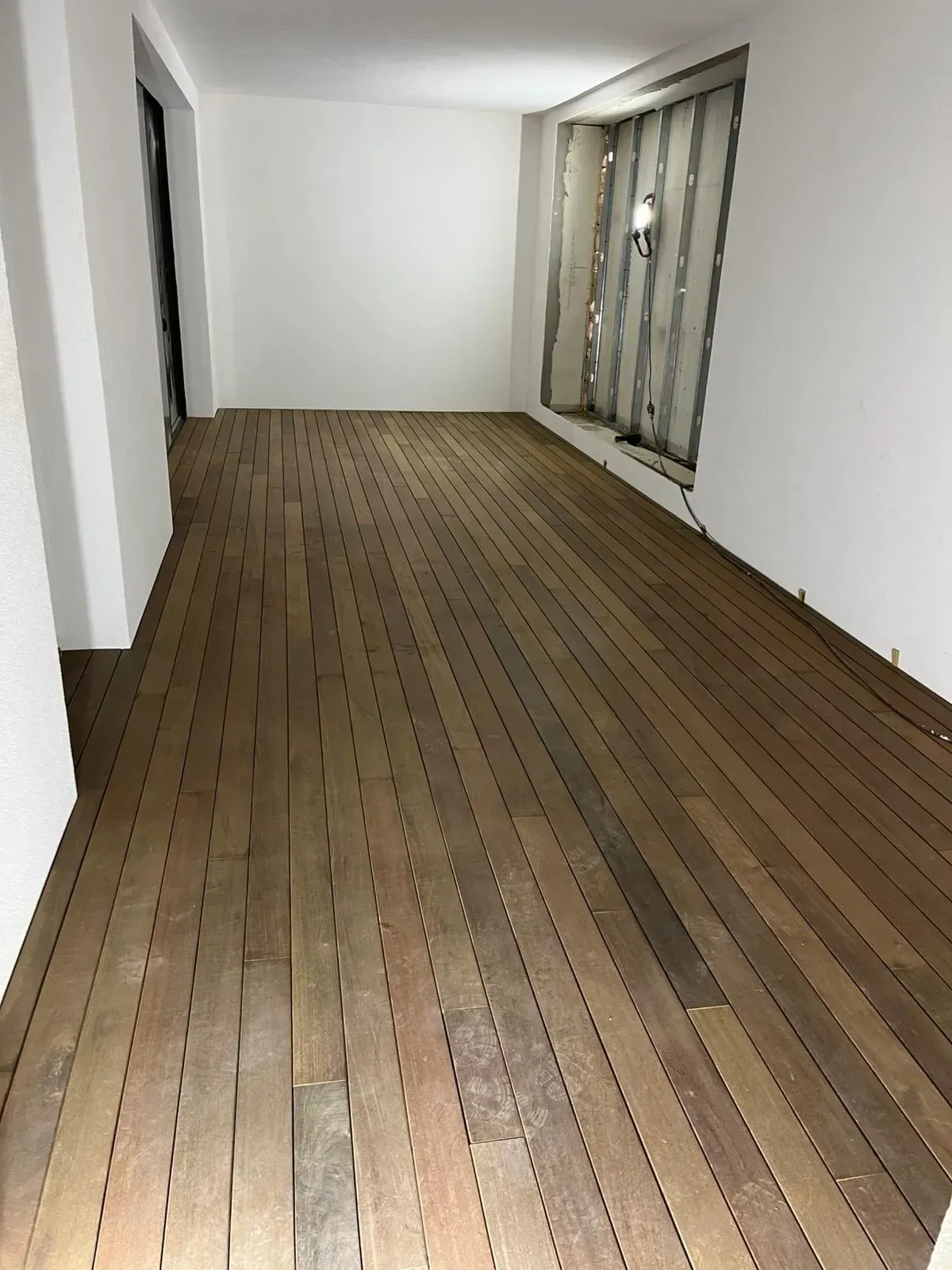 Habitación vacía con paredes blancas, suelo de madera y ventanas en el lado derecho.