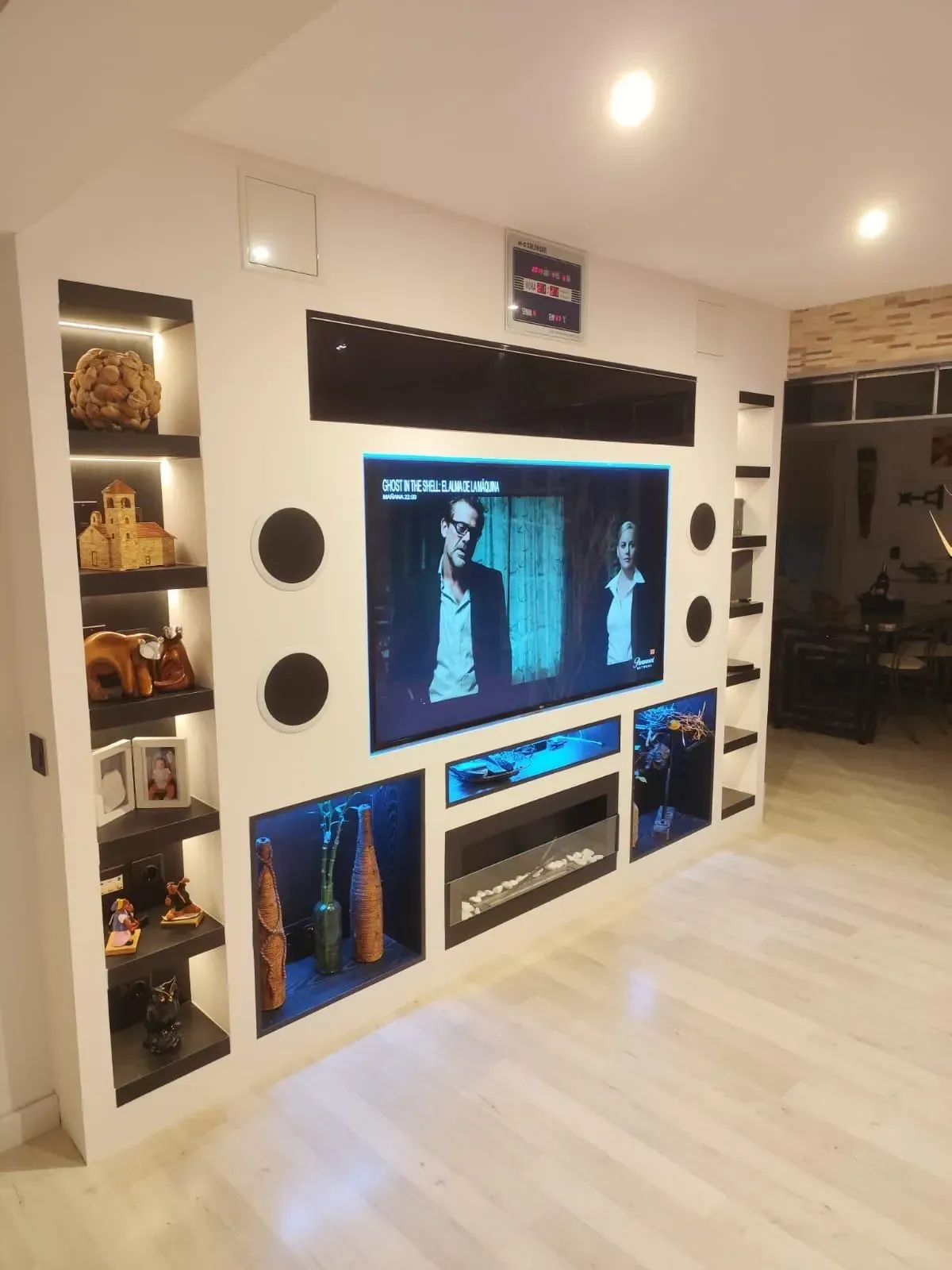 Sala de estar moderna con estanterías empotradas, un televisor grande y detalles de arte oscuro en una pared blanca.