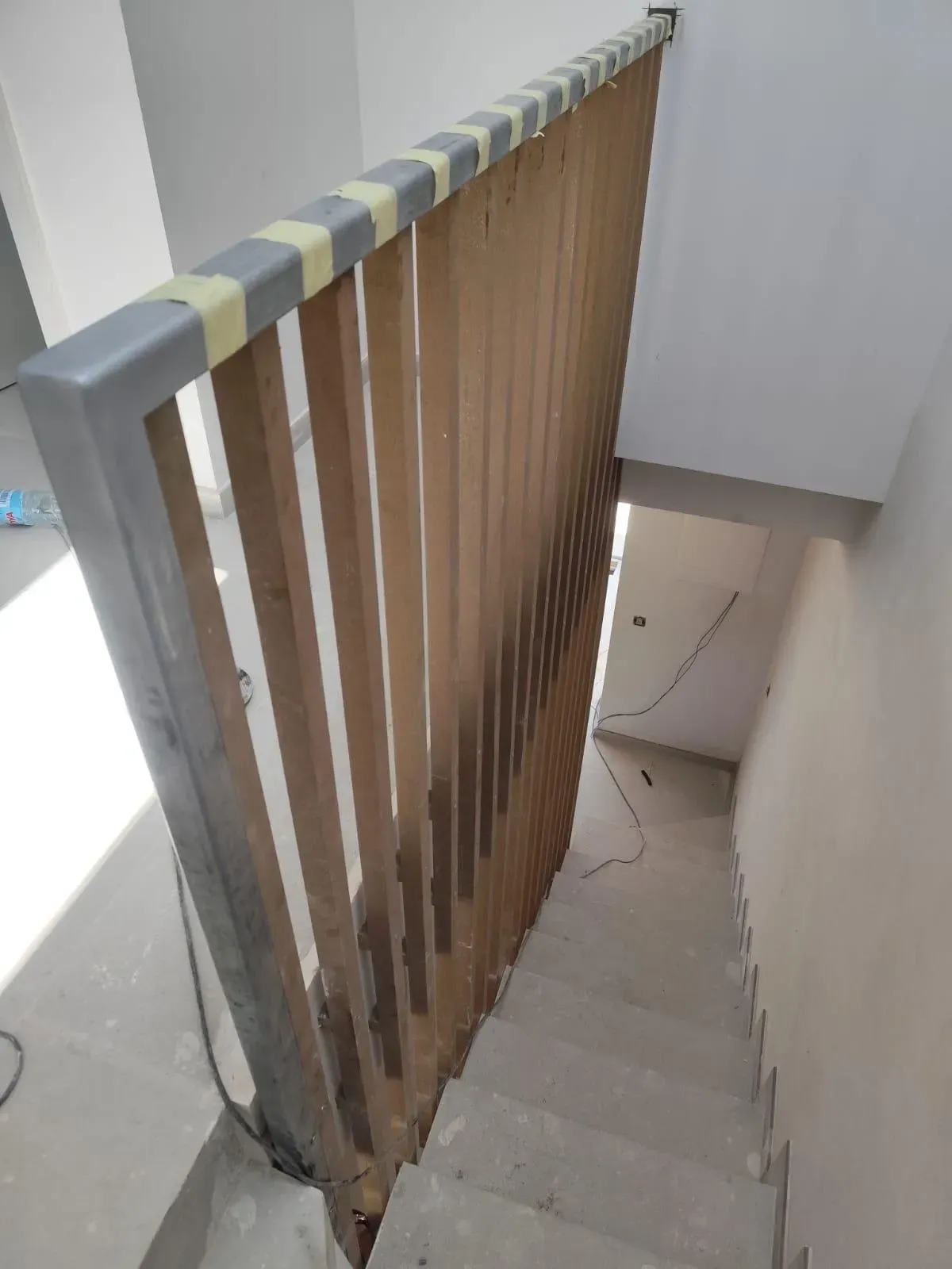 Escalera con barandilla de listones de madera y escalones grises en un espacio interior estrecho.