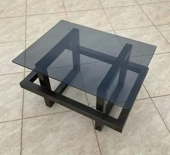 Mesa de centro con tablero de cristal oscuro y estructura de metal negro sobre suelo de baldosas.