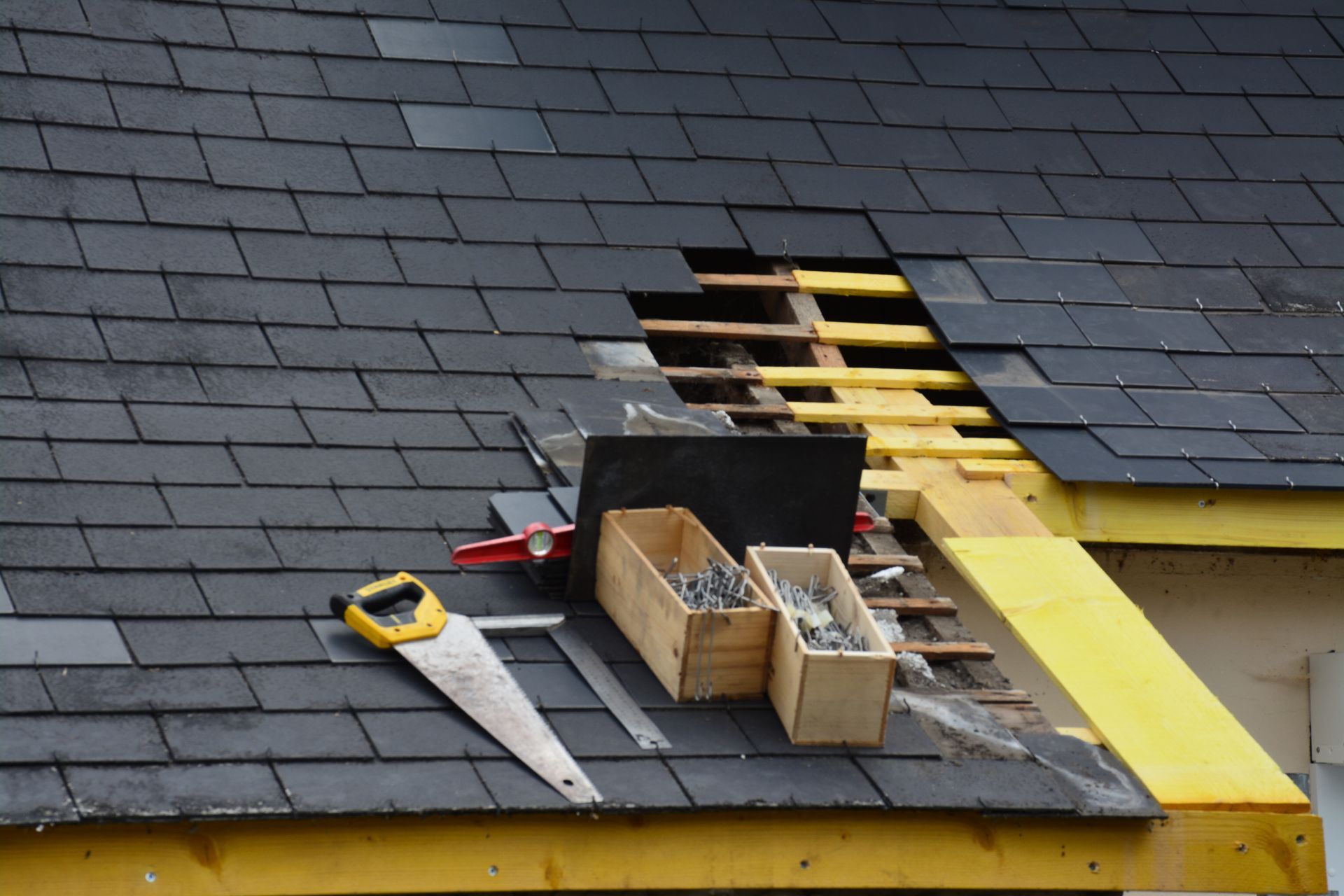 Réparation de toiture avec poutres en bois apparentes, outils et tuiles manquantes.