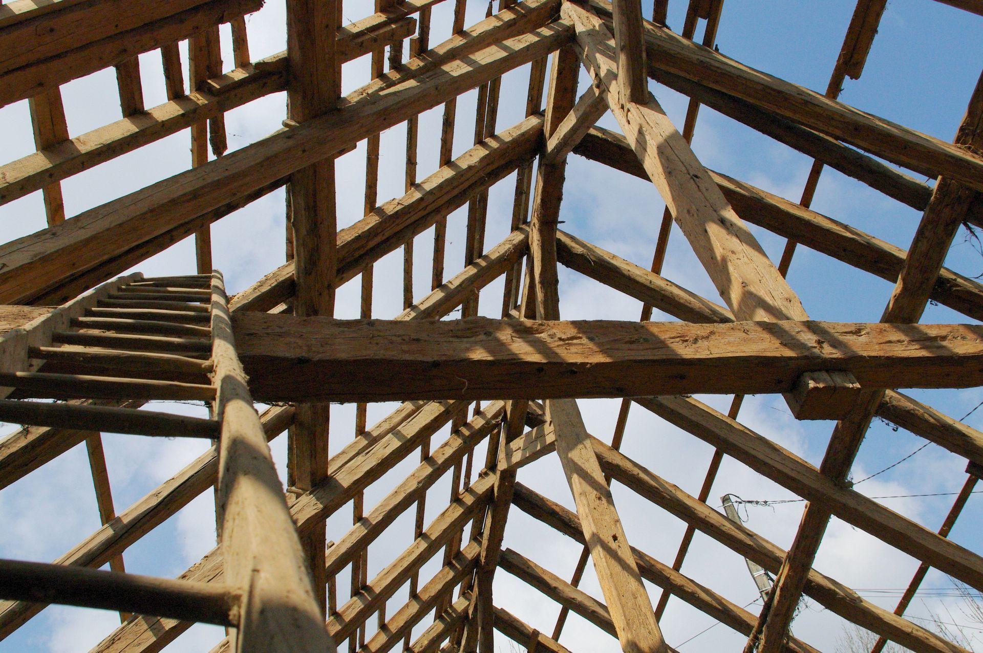 Charpente en bois avec échelle sur fond de ciel bleu.