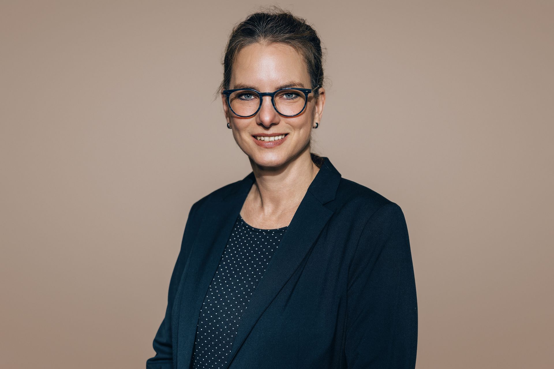 Eine Frau mit Brille und schwarzer Jacke lächelt in die Kamera.