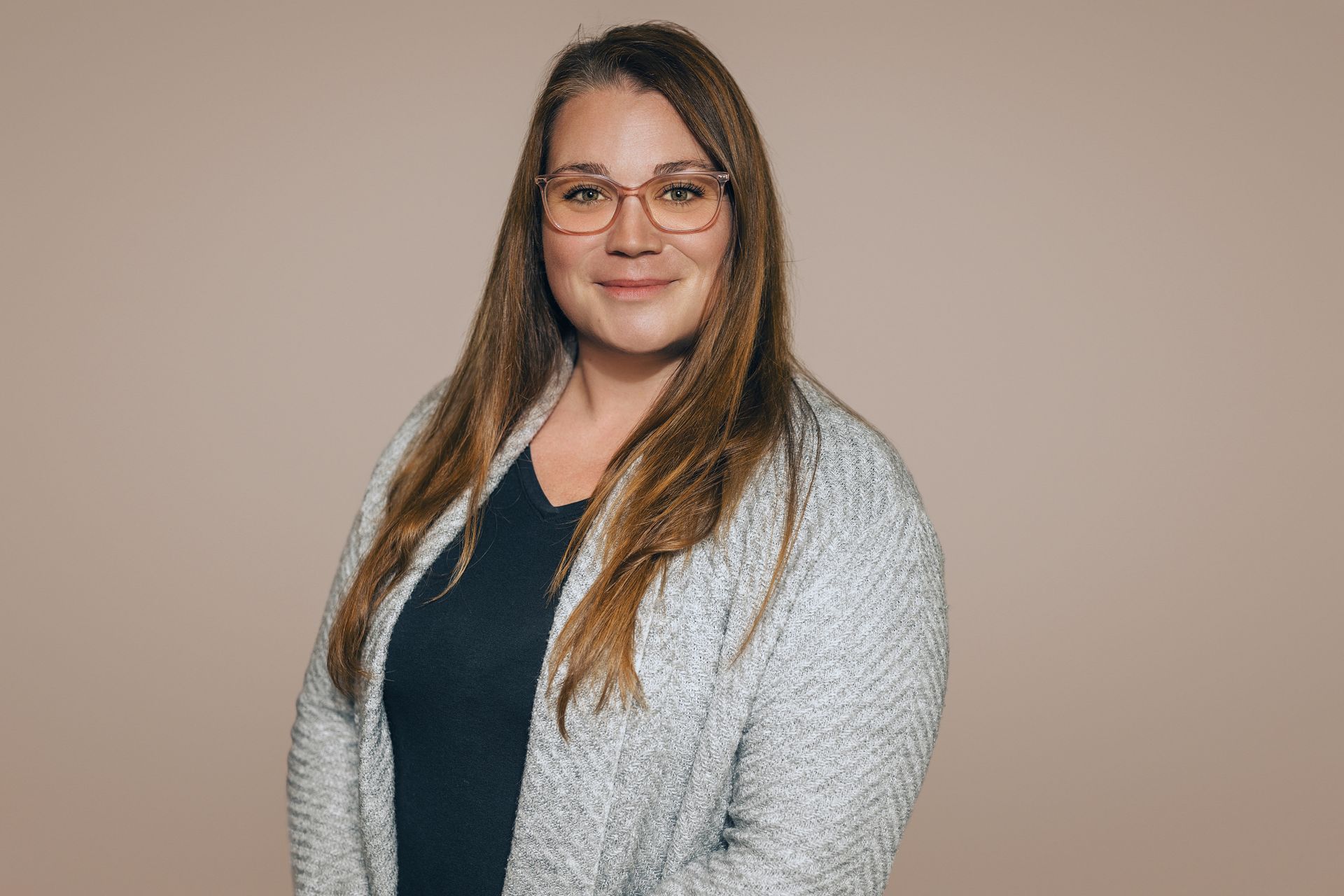 Eine Frau mit Brille und grauem Pullover lächelt in die Kamera.