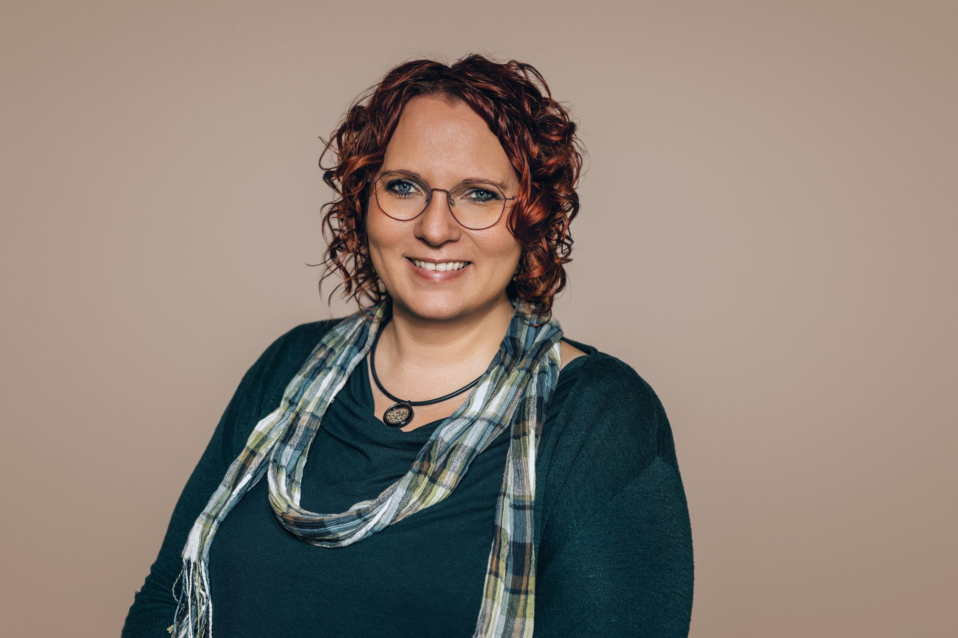 Eine Frau mit Brille und Schal lächelt in die Kamera.