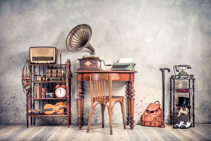 Phonographe sur un petit bureau, avec des meubles autour et des objets anciens tels qu'un réveil et un violon