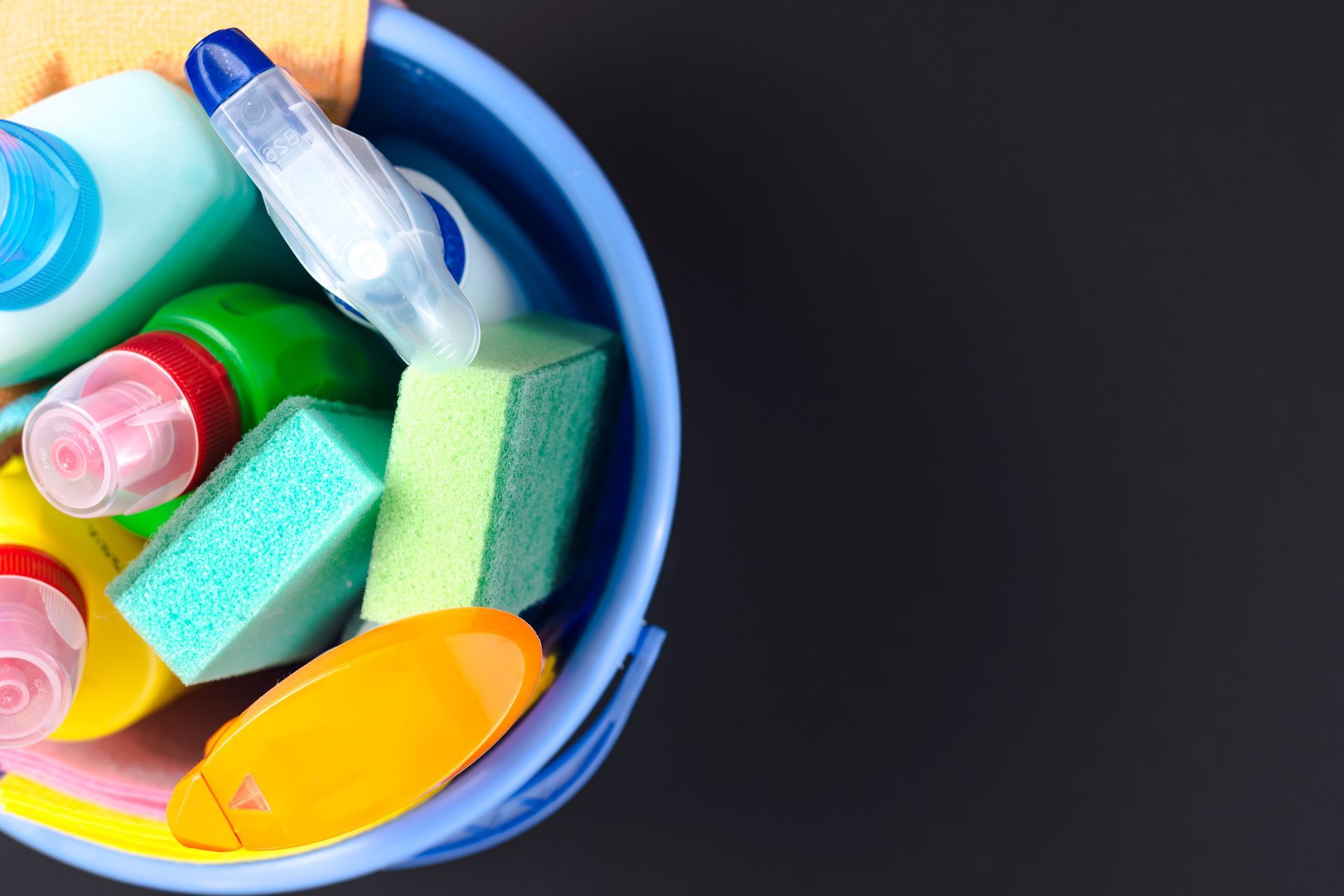 Un cubo azul lleno de productos de limpieza sobre un fondo negro.