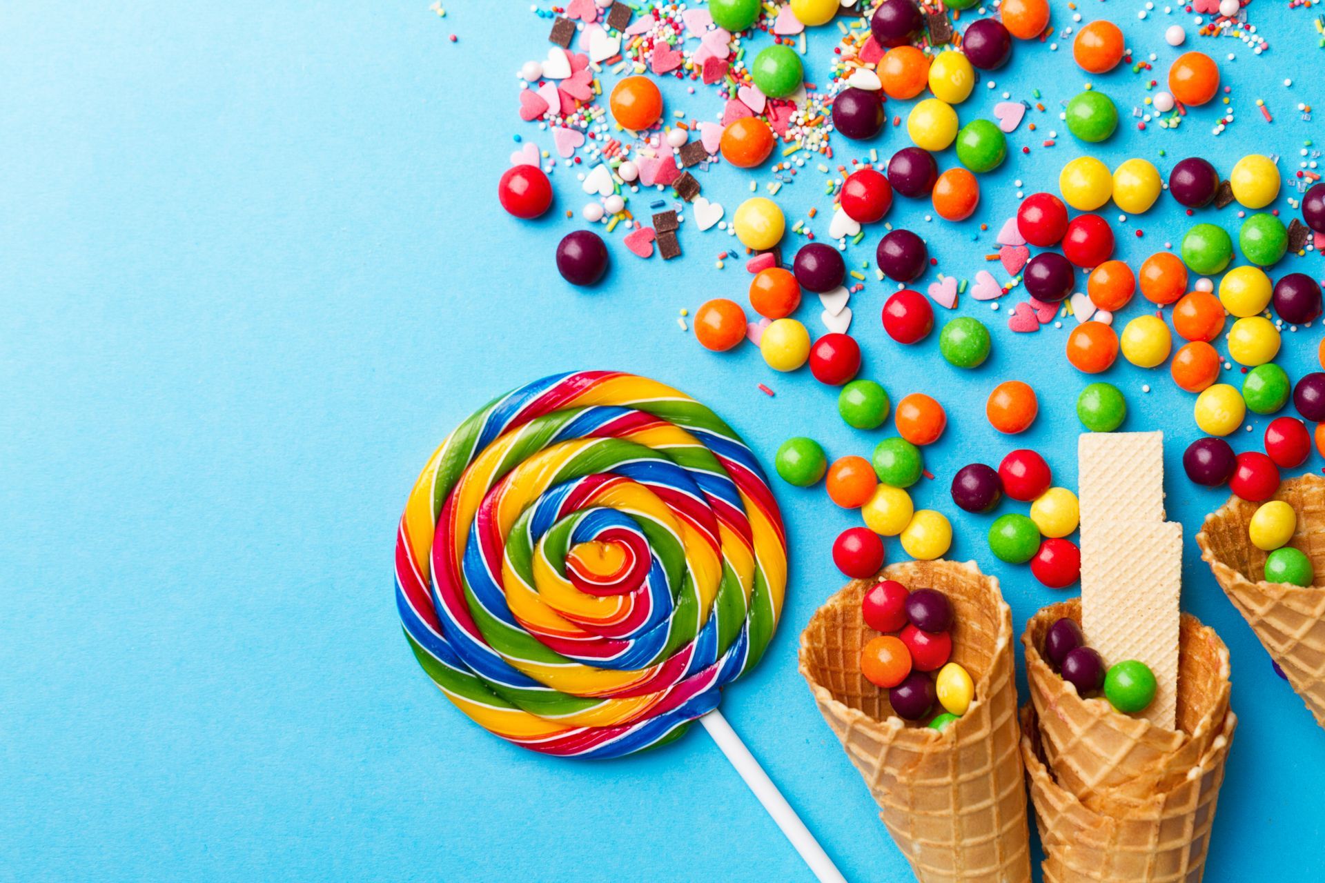 Una piruleta colorida, conos de helado llenos de dulces y chispas sobre un fondo azul.