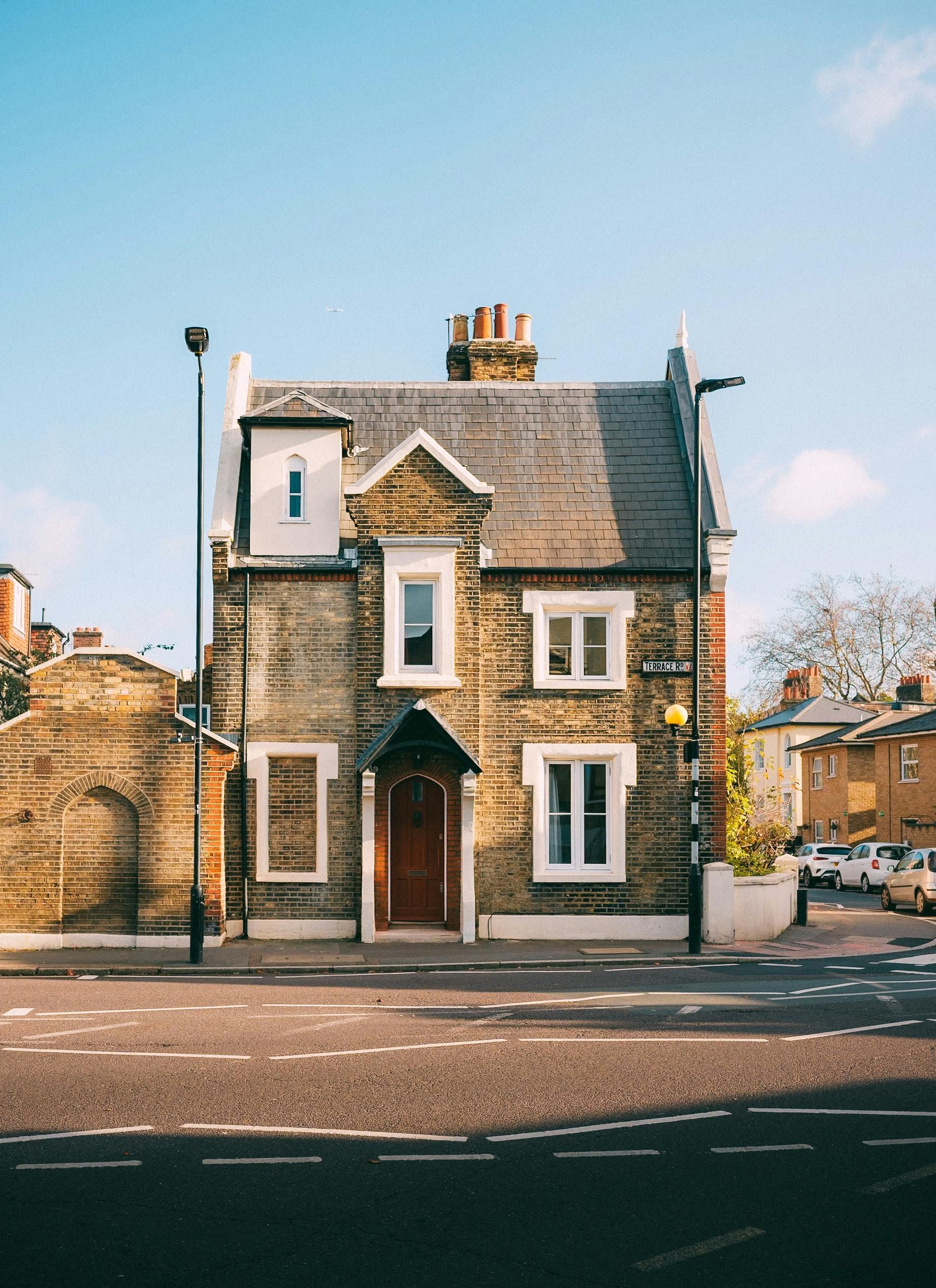 Maison en briques de deux étages avec une porte marron, des fenêtres à cadre blanc et un toit gris.