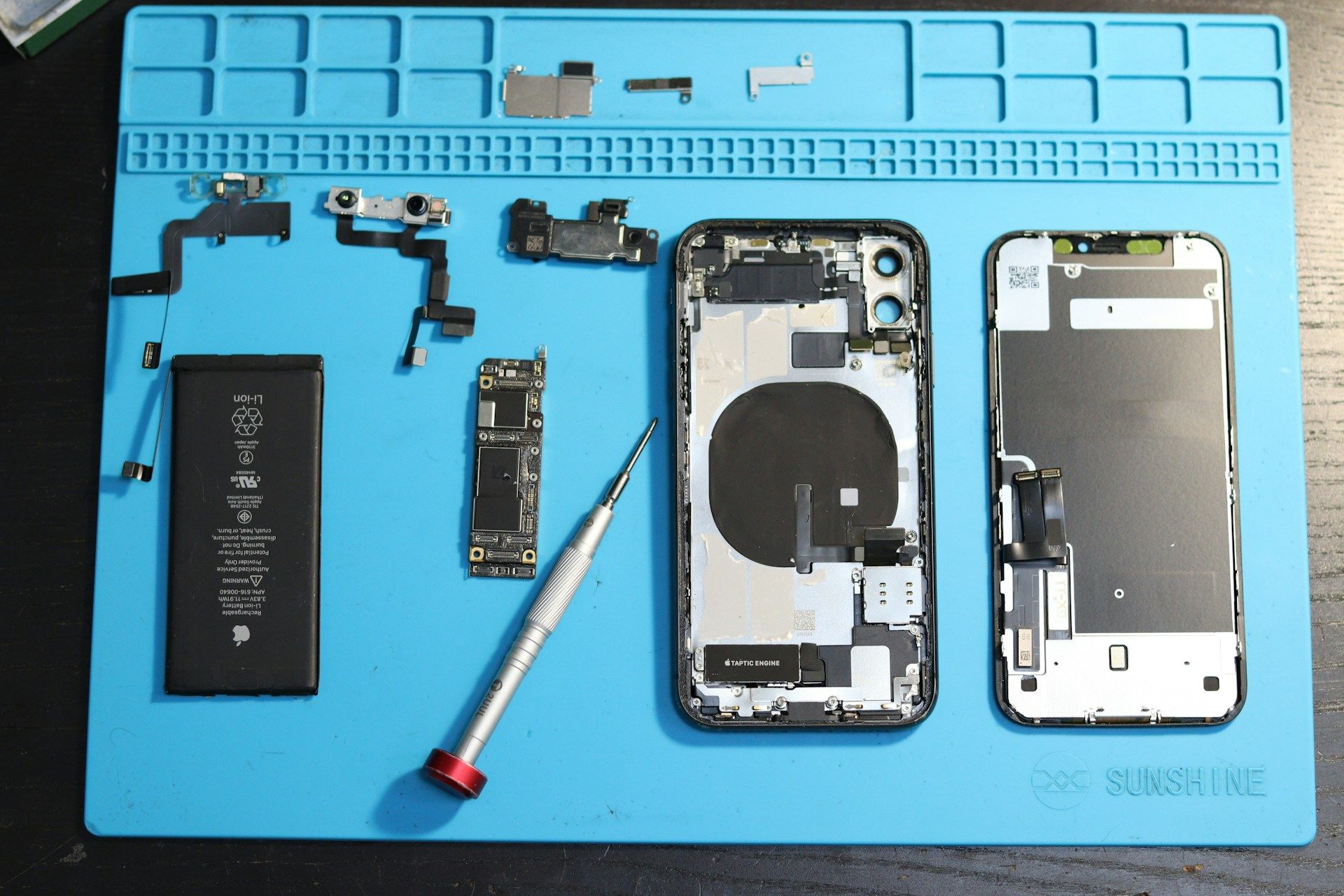 Pièces de smartphone démontées disposées sur un tapis de réparation bleu avec tournevis et outils