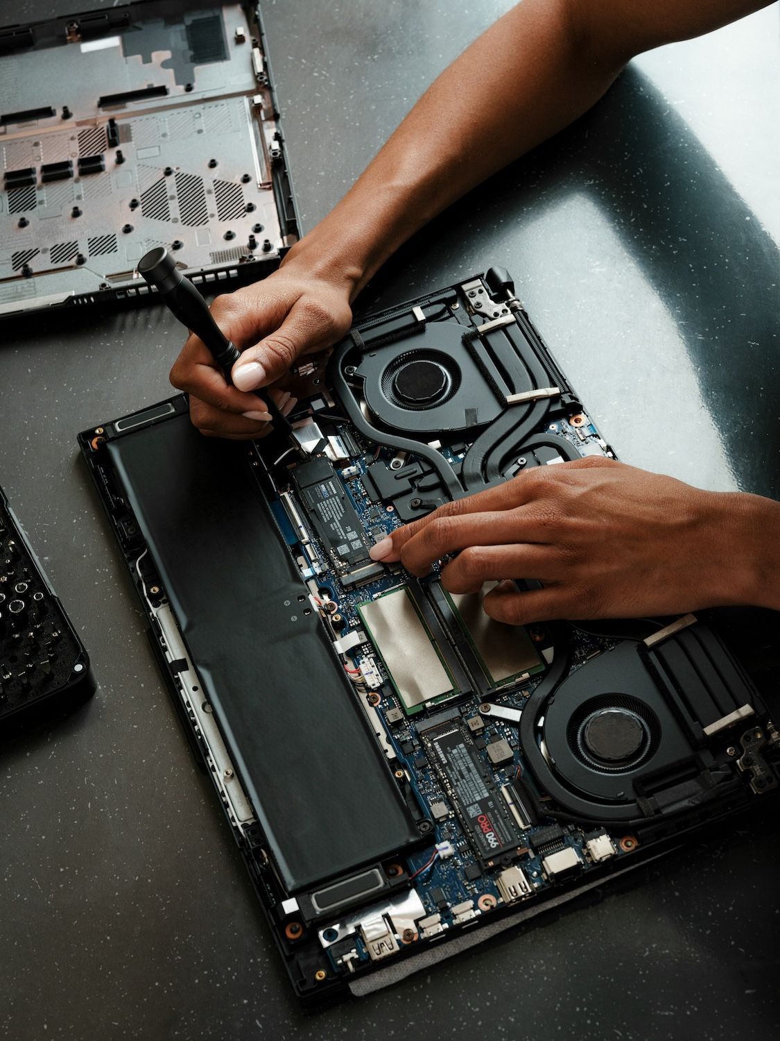 Des mains réparent les composants internes exposés d'un ordinateur portable sur un établi.