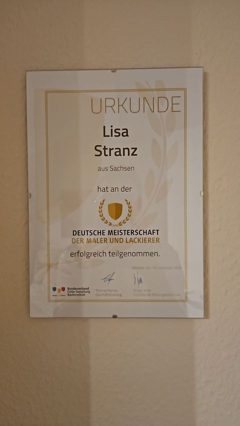Gerahmtes Poster an einer beigen Wand mit dem Namen „Lisa Stranz“ und einer goldenen Kreisgrafik.