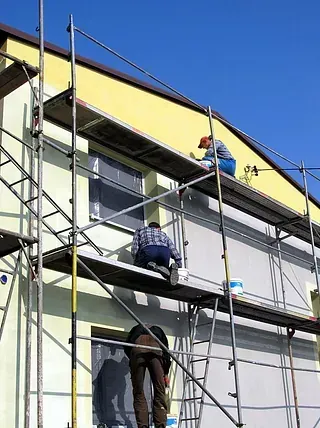 Dos hombres están pintando el costado de un edificio sobre un andamio.