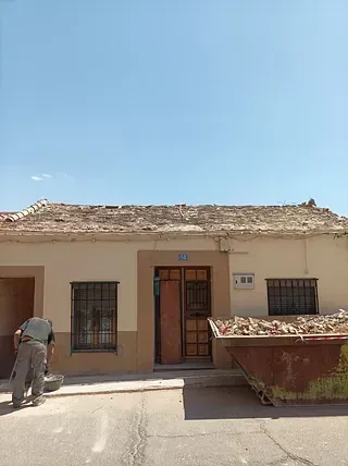 Un hombre está parado frente a una casa con un contenedor de basura delante de ella.