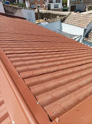 Un primer plano de un techo rojo con un edificio blanco al fondo.