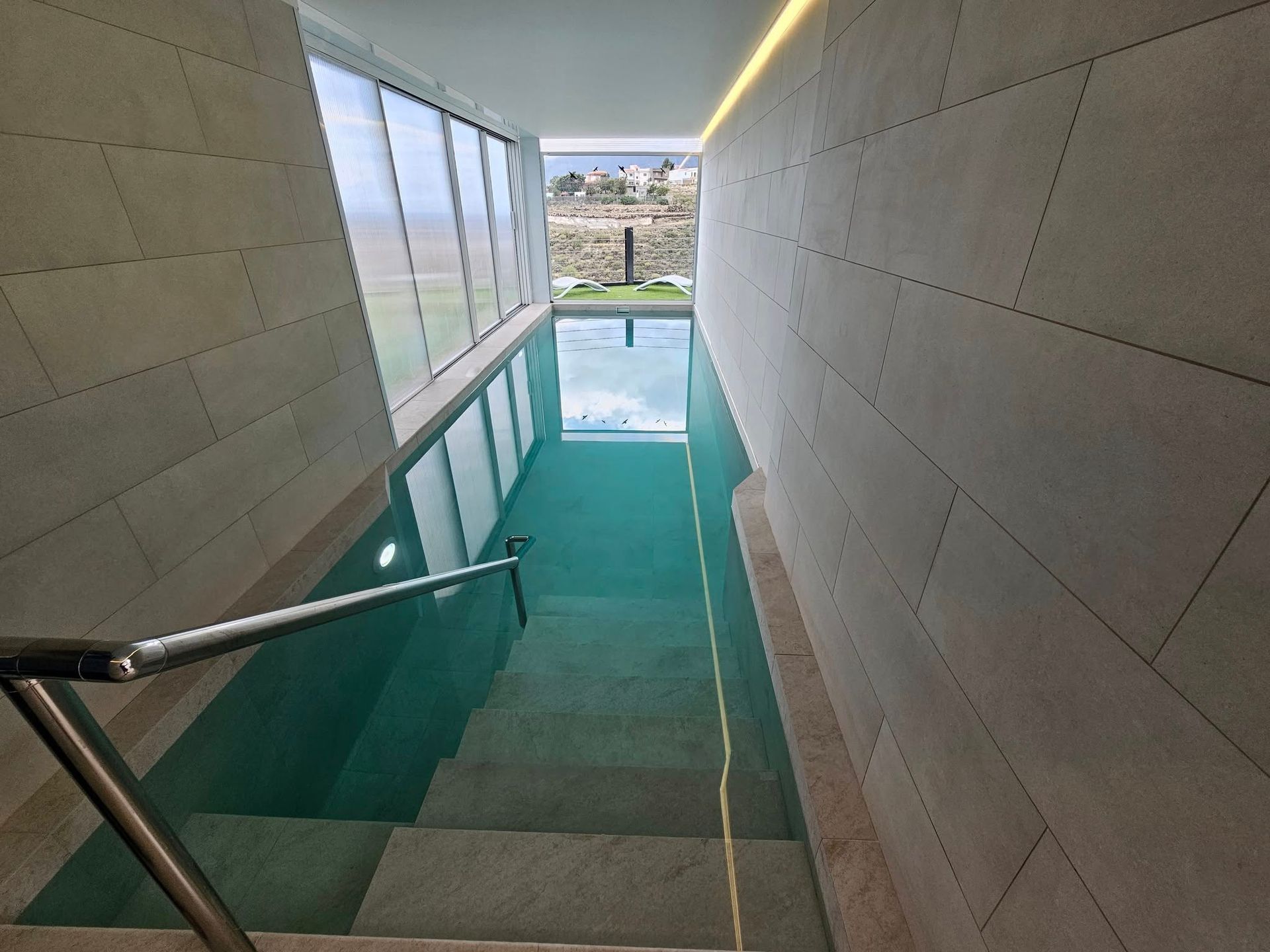 Una piscina cubierta estrecha con paredes de piedra y escalones que bajan, una barandilla